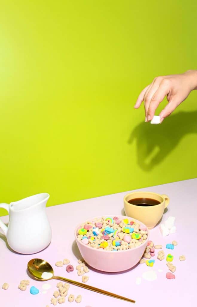 A vibrant breakfast setup with colorful cereal, coffee, and a playful hand dropping a marshmallow.