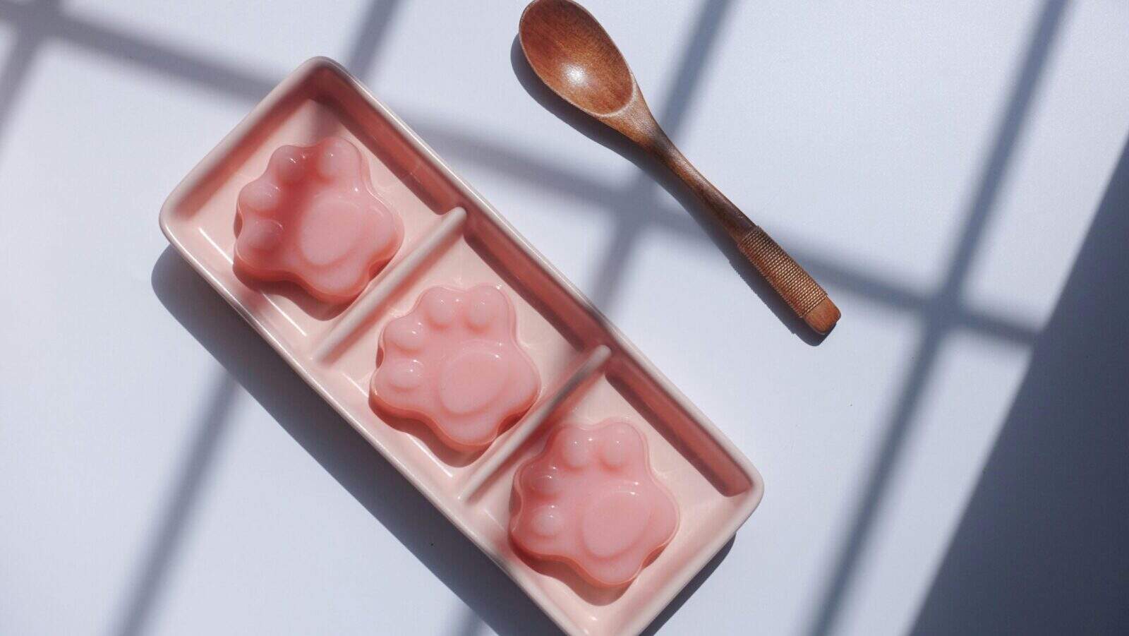 Three cute paw-shaped jellies on a pink tray with a wooden spoon, perfect for dessert lovers.
