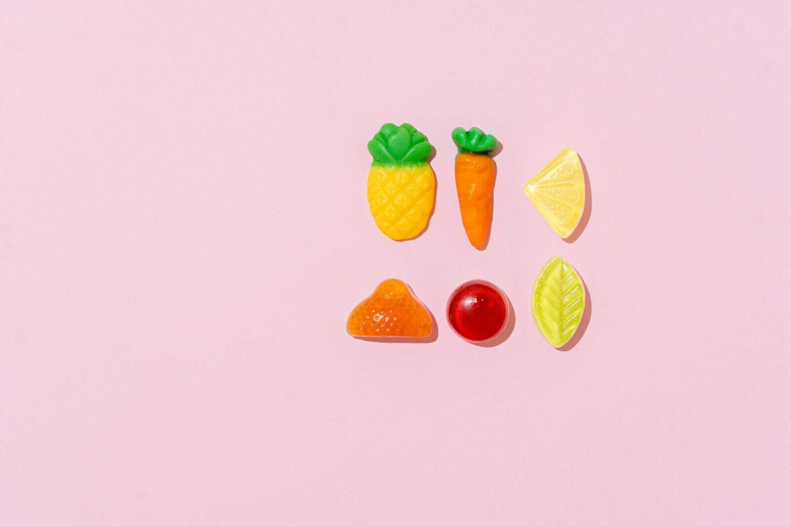 Top view of assorted fruit-shaped candies on a pastel pink background.