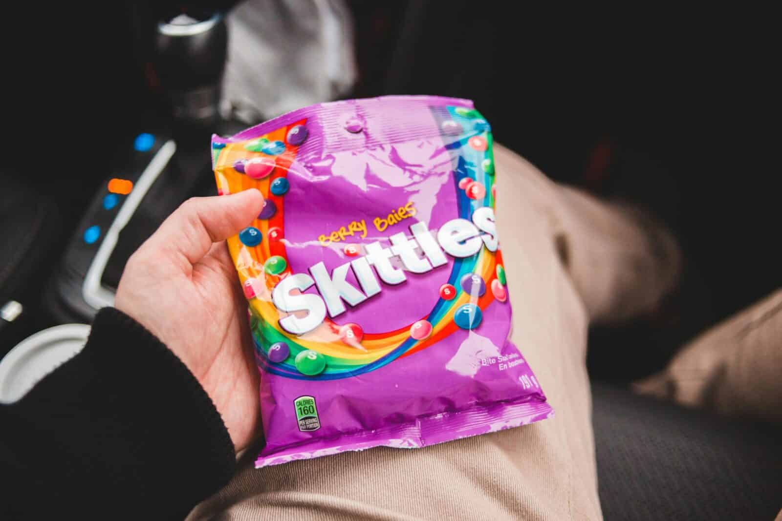 Person holding Skittles candy pack inside a car, showcasing vibrant colors and packaging.